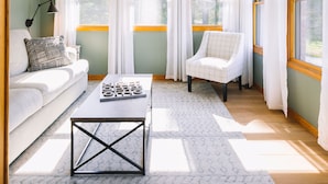 Une pièce dotée d’un ventilateur de plafond, d’un canapé, d’un fauteuil, d’une table basse et de grandes fenêtres avec des rideaux.