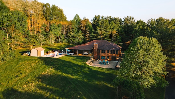 Une grande maison dotée d’un patio couvert, d’une piscine et d’un petit abri de jardin.