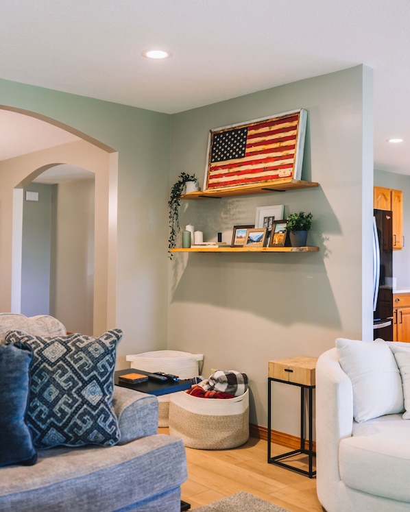 A living room with a sofa, a coffee table, and a TV. There is a wooden shelf with a flag and a plant.