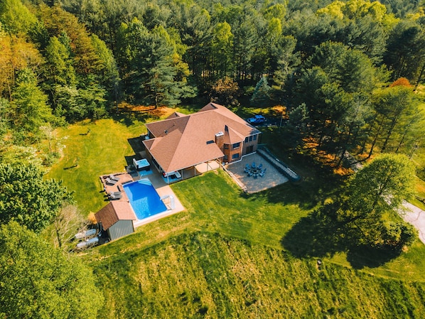 Vue aérienne d’une maison dotée d’une piscine, d’un patio et d’un grand jardin entouré d’arbres.