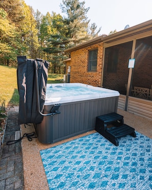 Ein Whirlpool in einem Hinterhof mit einem Backsteinhaus, einer Holzterrasse und einem blauen Teppich mit Muster.