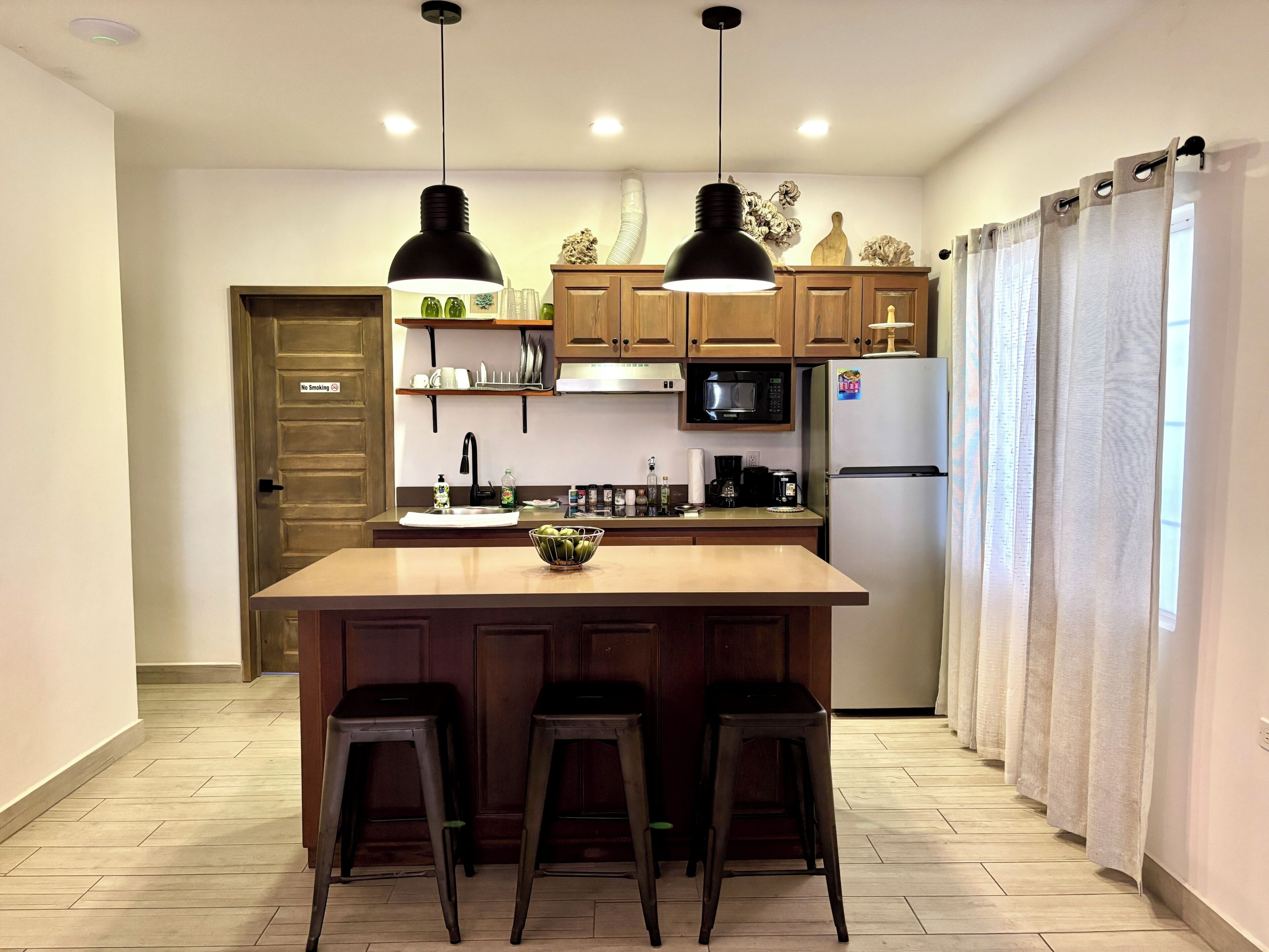 Una cocina con gabinetes de madera, una isla central con taburetes, un microondas y un refrigerador.