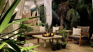 A cozy outdoor seating area with a wooden table, cushioned chairs, and various potted plants. - Stylish Apartments in Belize City (Belize City)