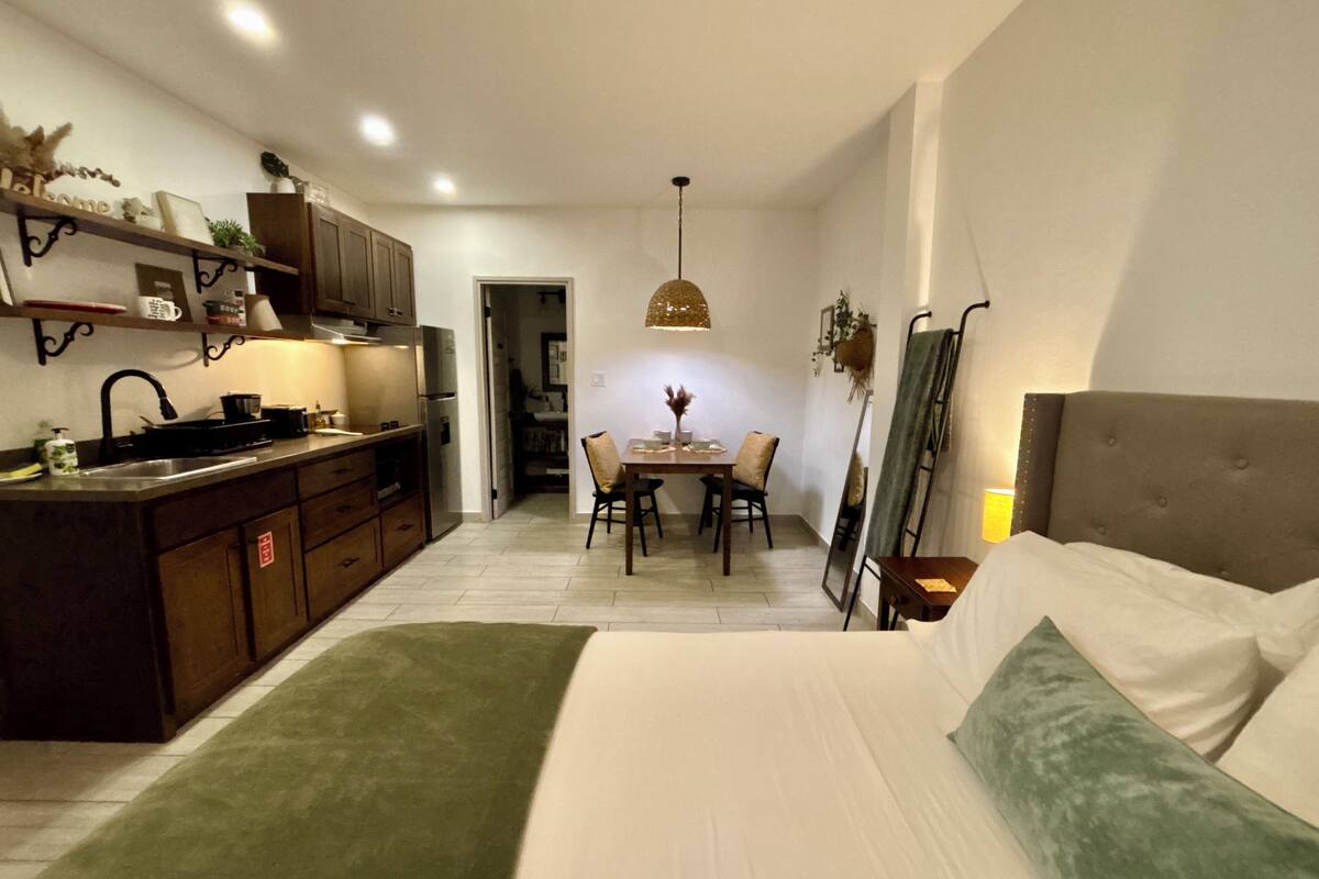 A compact hotel room with a kitchenette, a dining area, and a bed.