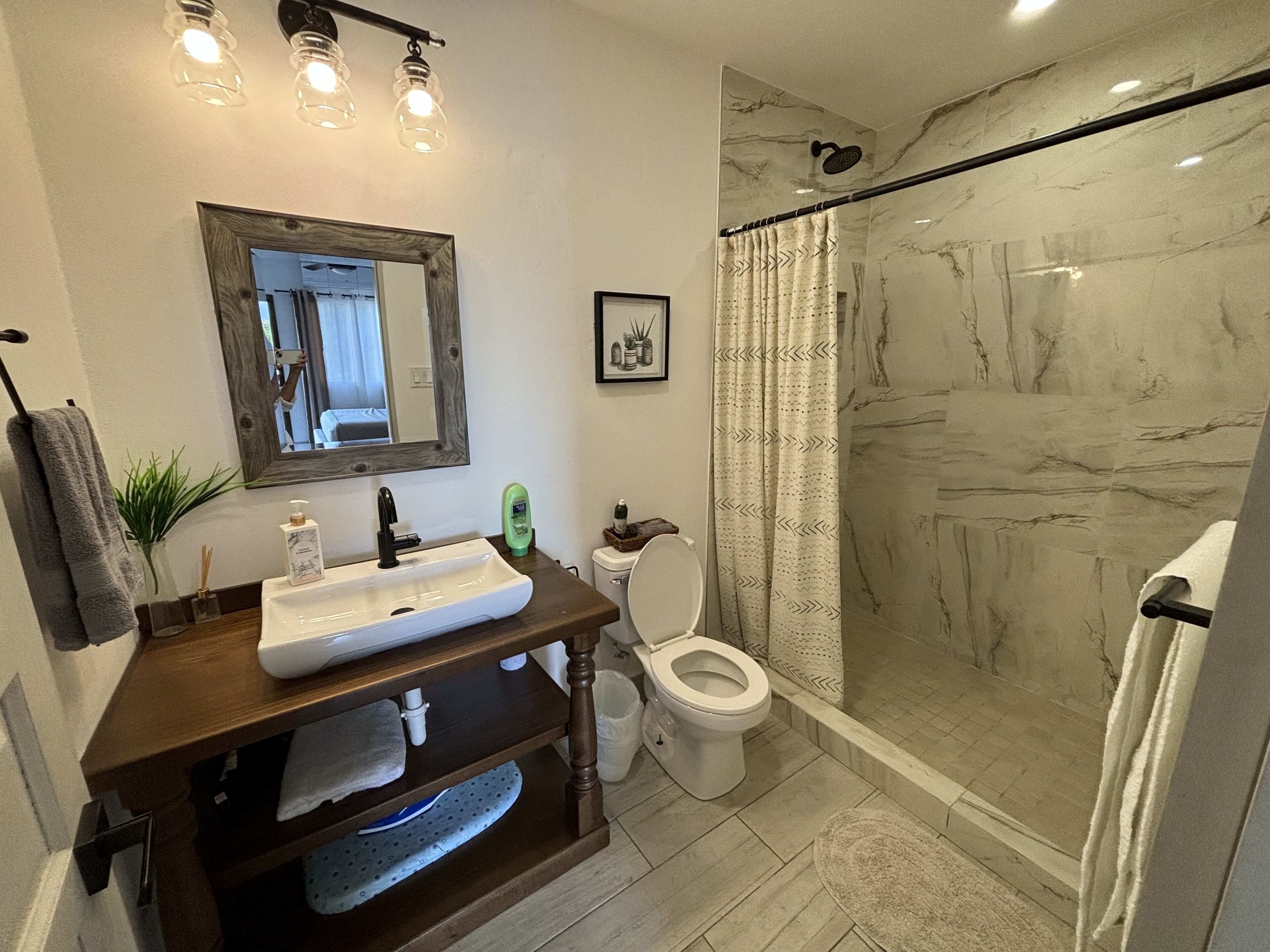 Un baño con ducha de mármol, lavabo con espejo y un inodoro.