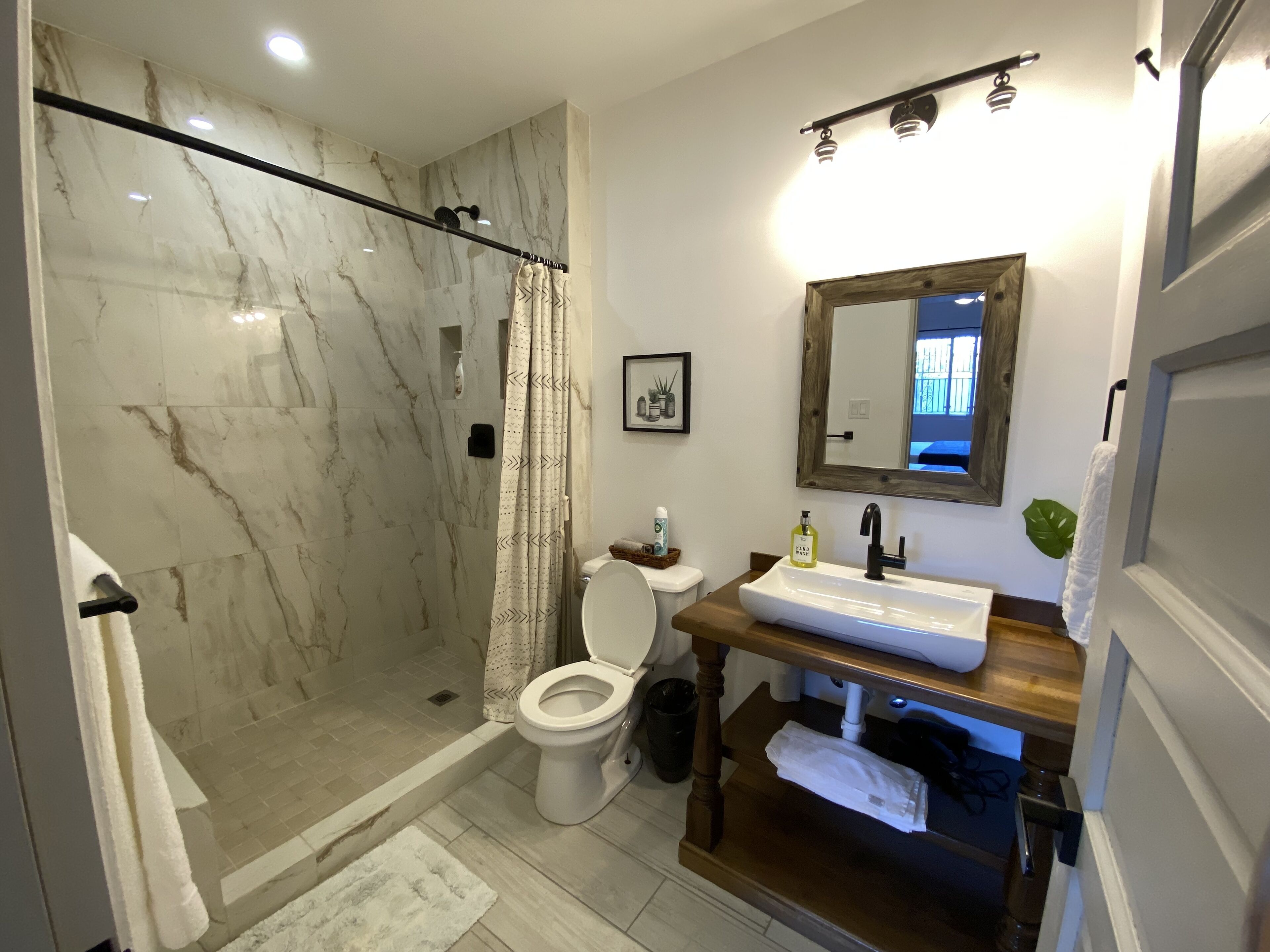 Un baño con ducha de vidrio, inodoro, lavamanos con espejo y tocador de madera.