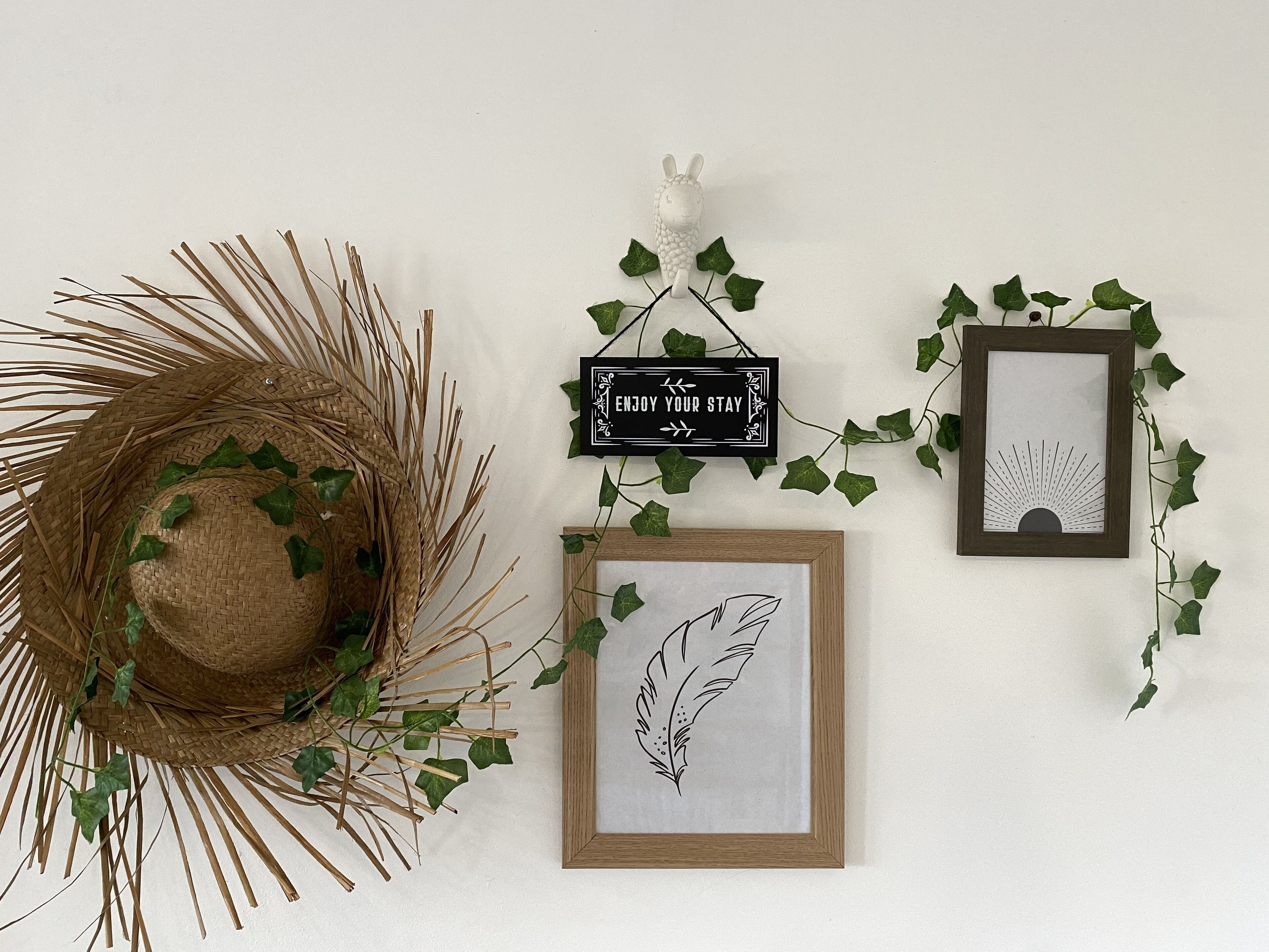Una parete con un cesto di vimini, un'opera d'arte con una piuma incorniciata, un disegno a raggiera incorniciato e un cartello con scritto 'ENJOY YOUR STAY'.