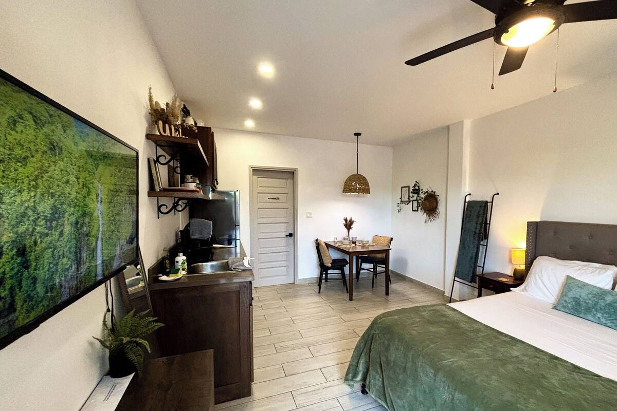 A bedroom with a bed, a desk with a computer, a dining table, and a ceiling fan.