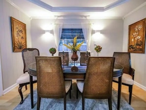 Un coin repas avec une table en verre entourée de chaises en osier, un vase rempli de fleurs et des lampes fixées au mur.