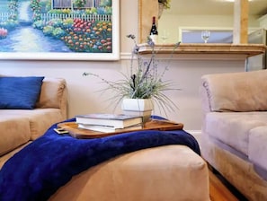 Un salon avec un canapé, une table basse ornée d’une plante et de livres, et un tableau accroché au mur.