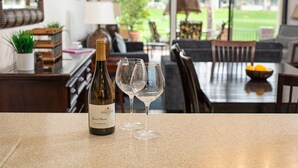 A bottle of wine and two glasses on a kitchen counter with a view of a dining area and outdoor space. - Palm Desert Private Retreat  (Palm Desert)