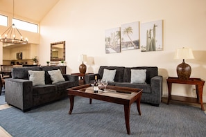 A spacious living room with two grey sofas, a wooden coffee table, and a chandelier.