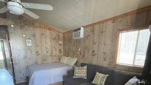 Et værelse med seng, sofa, loftventilator, airconditionanlæg, trævægge og et vindue.