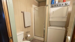Et lille badeværelse med toilet, bruseniche samt en stabling af vaskemaskine og tørretumbler.
