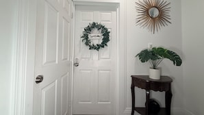 A white door with a 'welcome' sign, a sunburst mirror, and a potted plant. - Cozy Private Share Room (Englewood)