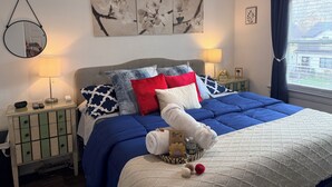 A neatly arranged bedroom with a blue bedspread, multiple pillows, a bedside lamp, a mirror, and artwork on the wall. - Cozy Private Share Room (Englewood)