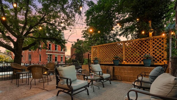 An outdoor seating area with wicker chairs and a patterned rug, a wooden lattice partition, and string lights. - Soulard Retreat. Fire Pit. Game Room. 3 Kings (St. Louis)
