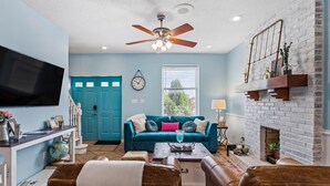 A living room with a blue sofa, brown leather chairs, a coffee table, a fireplace, a television, and a ceiling fan. - Soulard Retreat. Fire Pit. Game Room. 3 Kings (St. Louis)