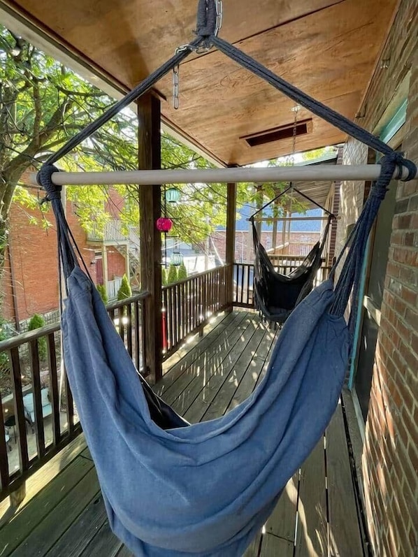 A hammock on a wooden porch with a view of a brick building and trees.