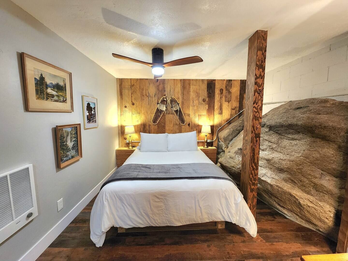 Une chambre à coucher avec un lit, des murs en bois, un ventilateur de plafond et des tableaux encadrés.