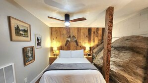 A bedroom with a bed, wooden walls, a ceiling fan, and framed pictures. - This fourplex is a 1 bedroom(s), 1 bathrooms, located in Shaver Lake, CA. (Shaver Lake)