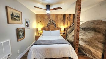 Une chambre à coucher avec un lit, des murs en bois, un ventilateur de plafond et des tableaux encadrés.