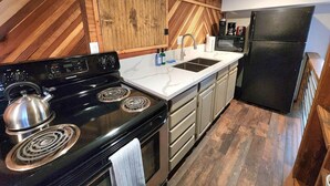 A kitchen with a black stove, white countertop, wooden cabinets, and a black refrigerator. - This fourplex is a 1 bedroom(s), 1 bathrooms, located in Shaver Lake, CA. (Shaver Lake)