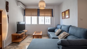 A modern living room with a sofa, a TV on a wooden stand, and a small table. - Apartment Tribalia - Cadiz beaches (Cádiz)