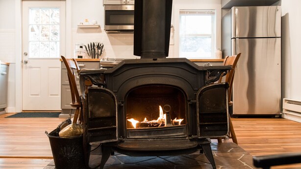 A stone-floored kitchen with a wood-burning stove, a stainless steel refrigerator, and a window.