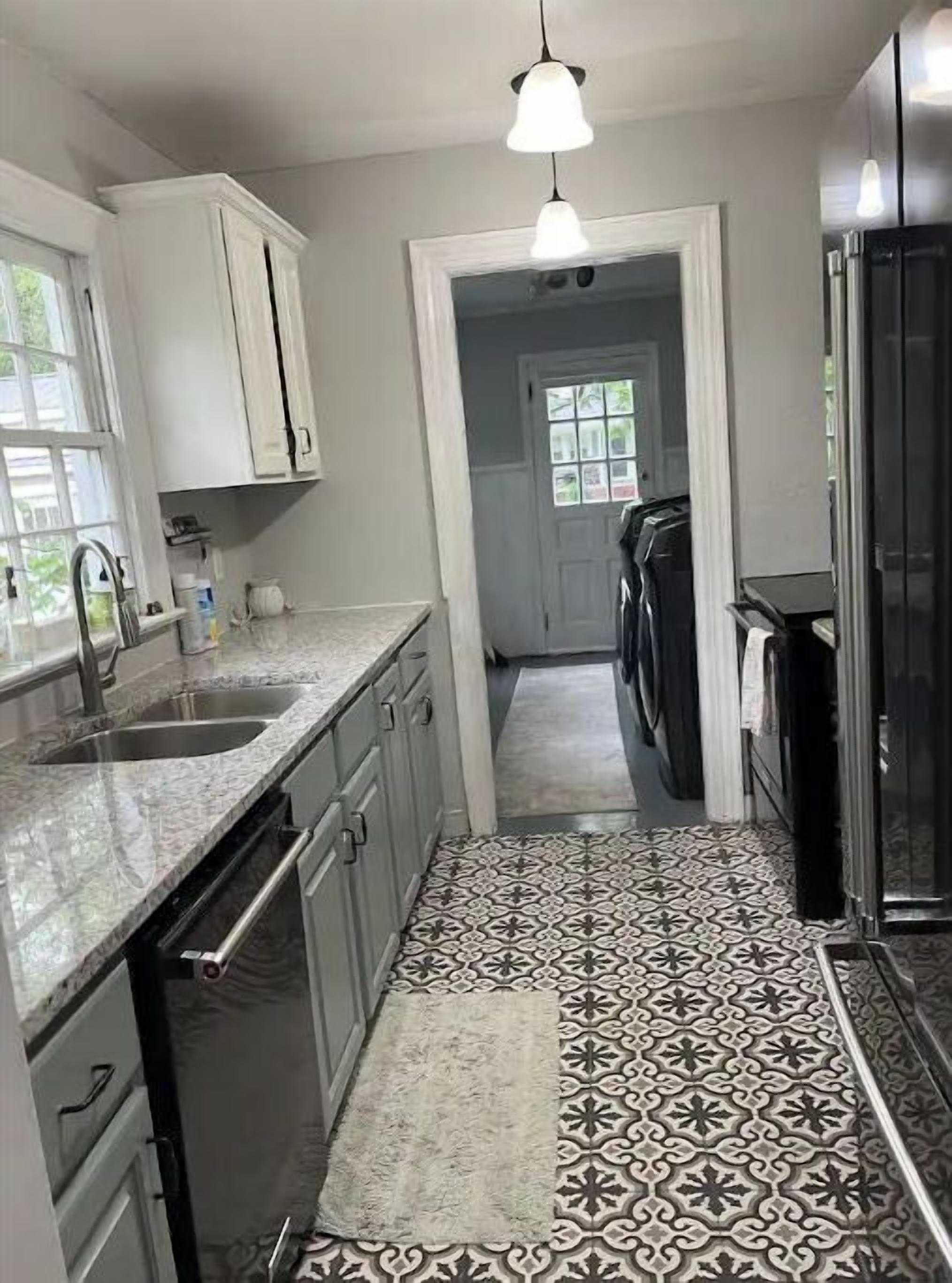 A kitchen with white cabinets, a granite countertop, a patterned tile floor, and a hanging light fixture.
