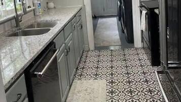 A kitchen with white cabinets, a granite countertop, a patterned tile floor, and a hanging light fixture.