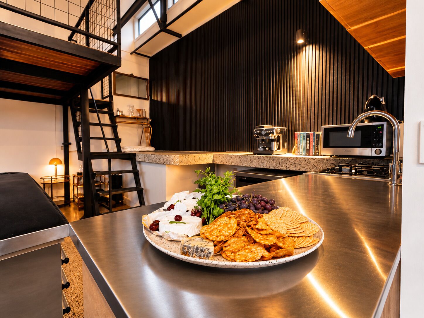 Een moderne keuken met roestvrijstalen apparatuur, een houten trap en een eethoek met een bord eten.