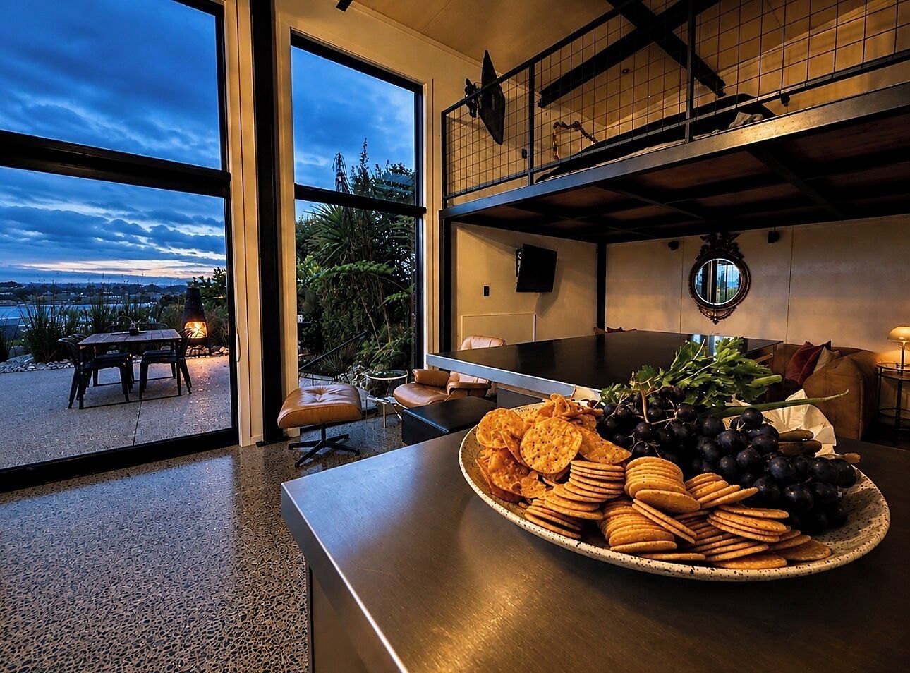 Un interior moderno con comedor que presenta una abundante bandeja de bocadillos y uvas, vistas al exterior y una acogedora zona de estar.