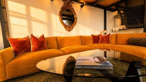 A modern living room with a curved sofa, a glass coffee table, and a large mirror on the wall. - Eco Lux Mapua | Inlet Views, Outdoor Bath & Fire (Mapua)