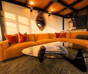 A modern living room with a curved sofa, a glass coffee table, and a large mirror on the wall. - Eco Lux Mapua | Inlet Views, Outdoor Bath & Fire (Mapua)