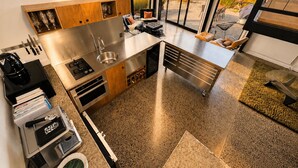 A modern kitchen with a large island, stainless steel appliances, and a view of a lake. - Eco Lux Mapua | Inlet Views, Outdoor Bath & Fire (Mapua)