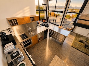 A modern kitchen with a large island, stainless steel appliances, and a view of a lake. - Eco Lux Mapua | Inlet Views, Outdoor Bath & Fire (Mapua)