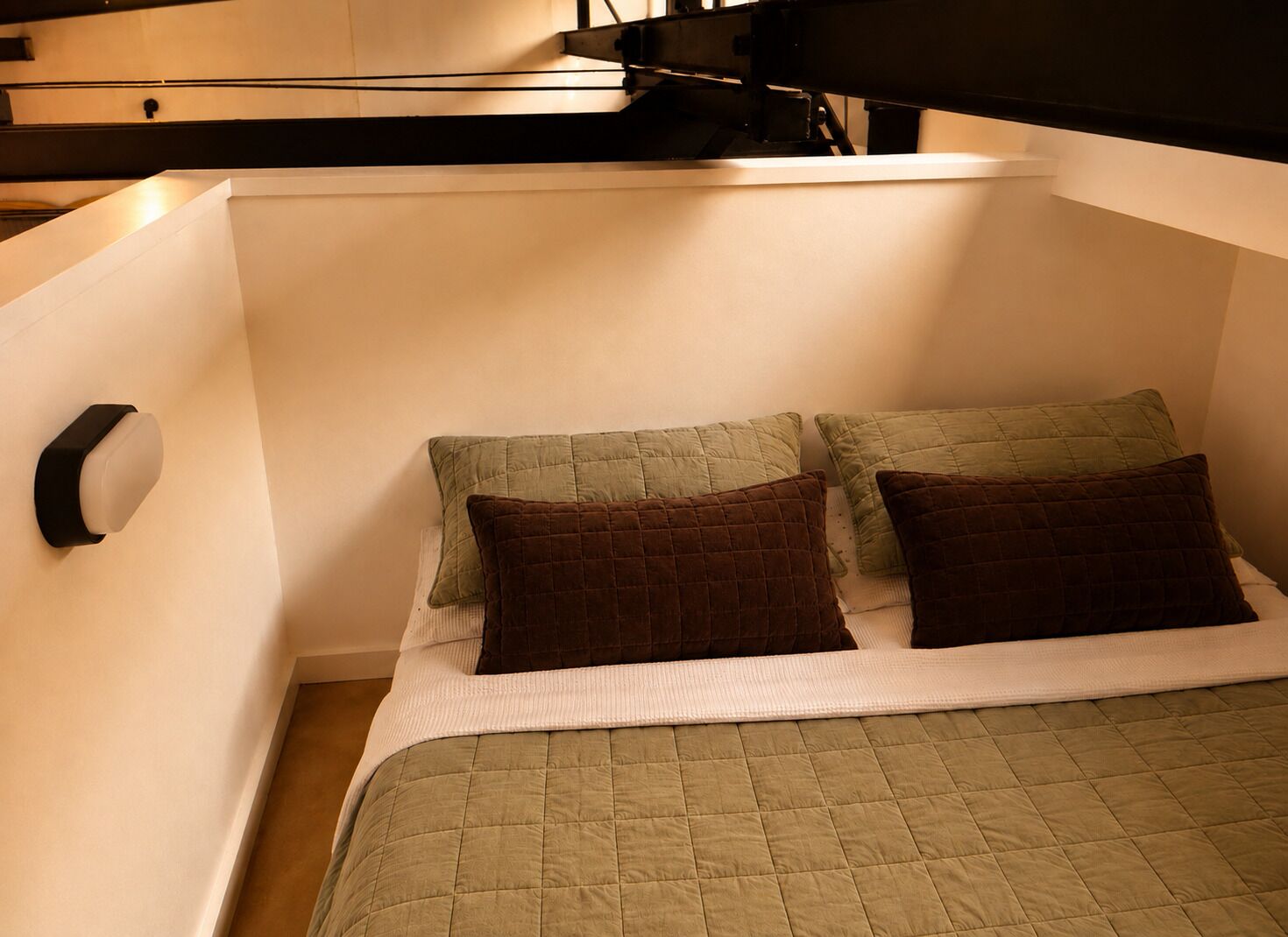 Une chambre compacte avec un lit simple, une couette matelassée verte, deux oreillers et un mur blanc.