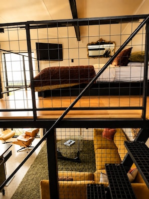 A bunk bed with a mattress and pillows, a desk with a chair, a small table, and a sofa with cushions. - Eco Lux Mapua | Inlet Views, Outdoor Bath & Fire (Mapua)
