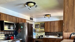 A modern kitchen with wooden cabinets, a stainless steel refrigerator, a microwave, and a large island with bar stools. - Quiet Eco-Friendly Home Close to Downtown & Desert—Wildlife in Abundance! (Tucson)