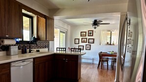 A modern kitchen with wooden cabinets, a dishwasher, and a refrigerator. There is a dining area with a table and chairs, and a hallway leading to a living room. - Quiet Eco-Friendly Home Close to Downtown & Desert—Wildlife in Abundance! (Tucson)