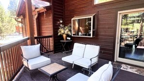 A wooden deck with white outdoor furniture, a small table, and a potted plant.