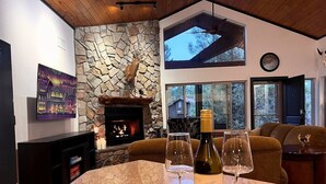 A kitchen with a stone fireplace, a dining area with a table and chairs, and a living room with a couch and a TV.