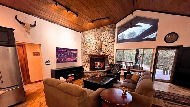 A cozy living room with a stone fireplace, a large window, and a modern kitchen area.