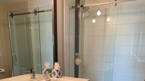 Une salle de bain moderne avec une douche à l’italienne en verre, un grand miroir et un meuble-lavabo blanc doté de deux vasques.