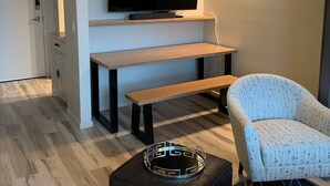 Un salon moderne avec un téléviseur à écran plat, un banc, un fauteuil à motifs et un petit pouf.