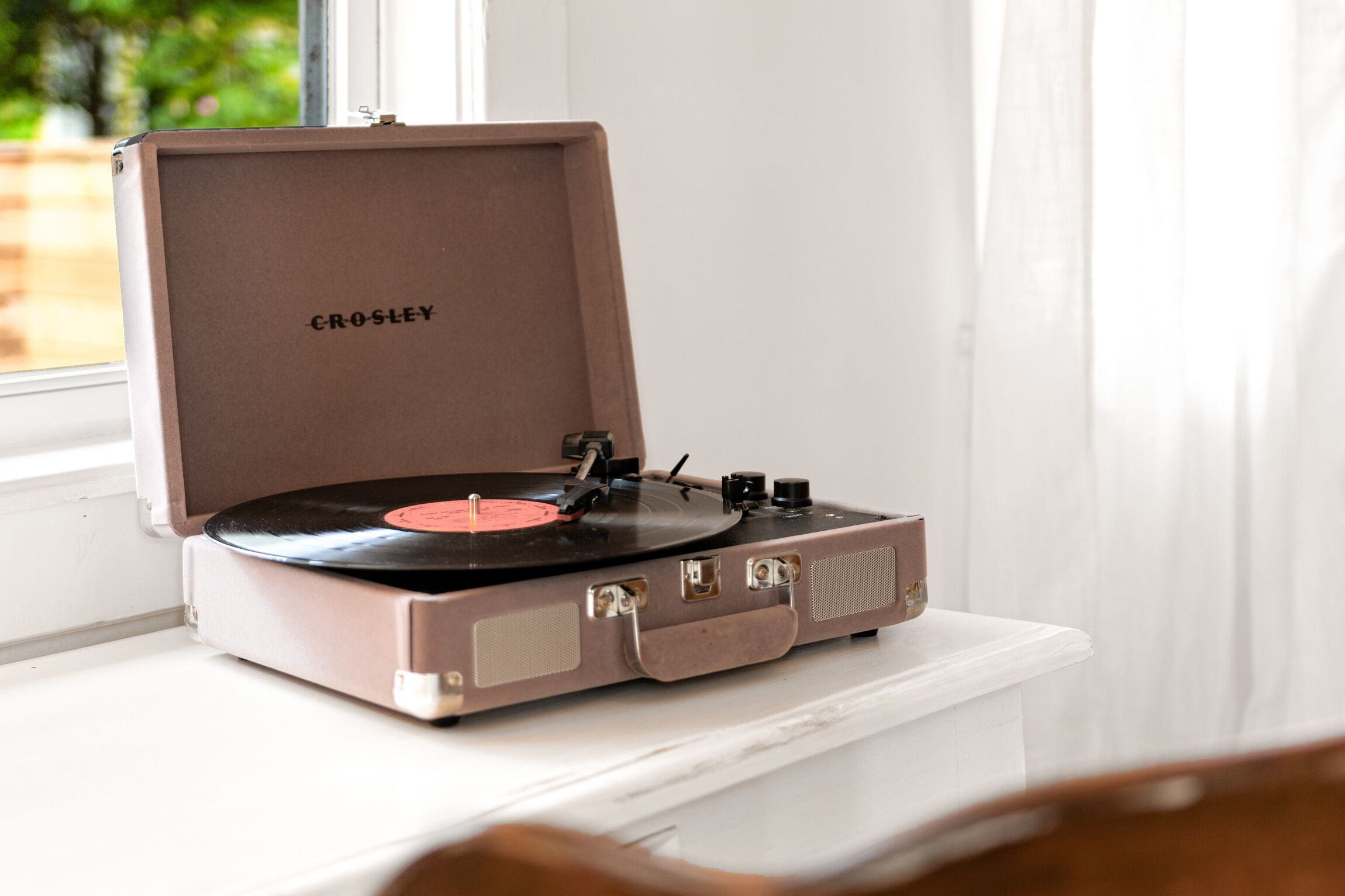 Ein Crosley-Kofferplattenspieler auf einem weißen Tisch in der Nähe eines Fensters.