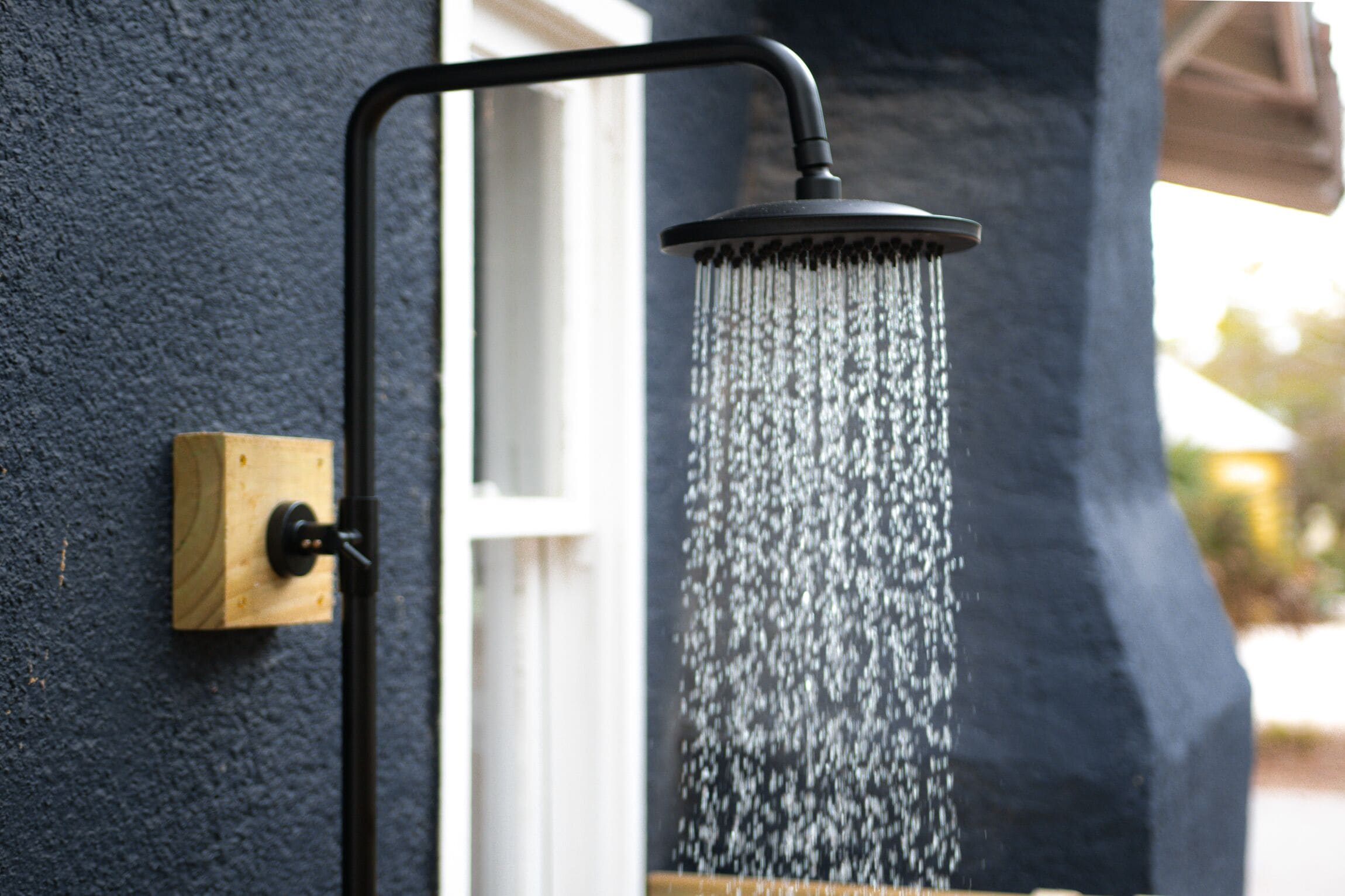 A showerhead with water flowing from it, mounted on a wall next to a window.