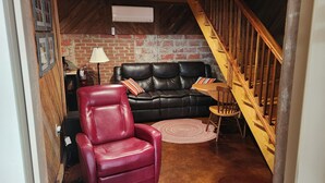 A cozy living room with a red leather chair, a black leather sofa, and a wooden staircase.
