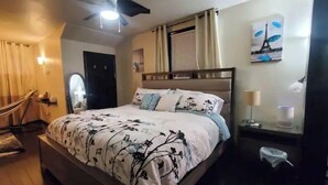 A bedroom with a bed, a ceiling fan, a nightstand, a lamp, and a painting of the Eiffel Tower.